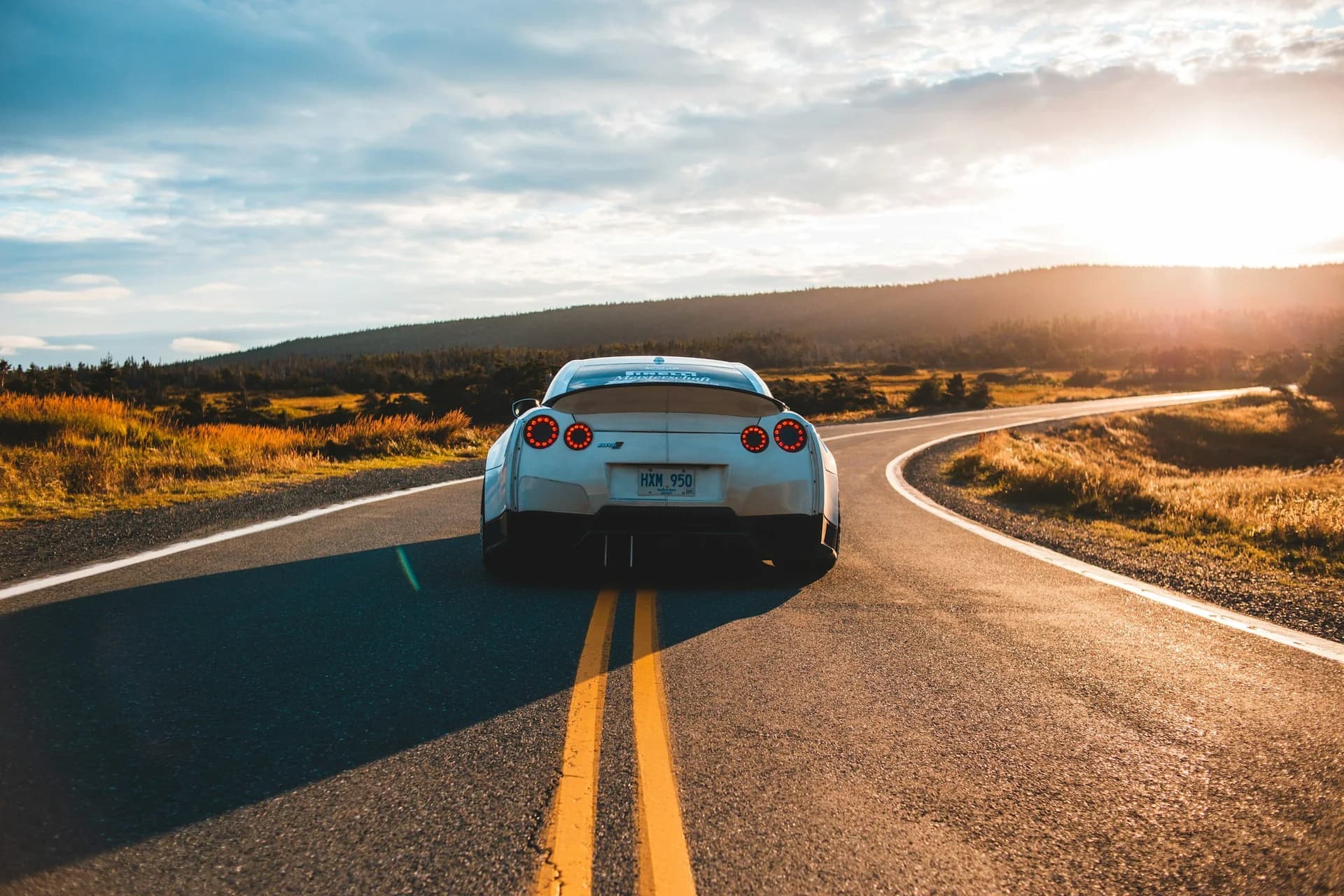 Baltas sportinis automobilis kelyje saulėlydžio metu